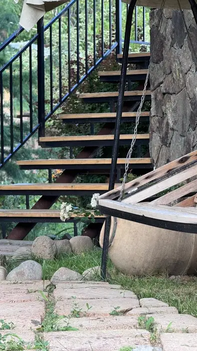 Wooden stairs up to the rooms, beside a swing seat and an old clay karas